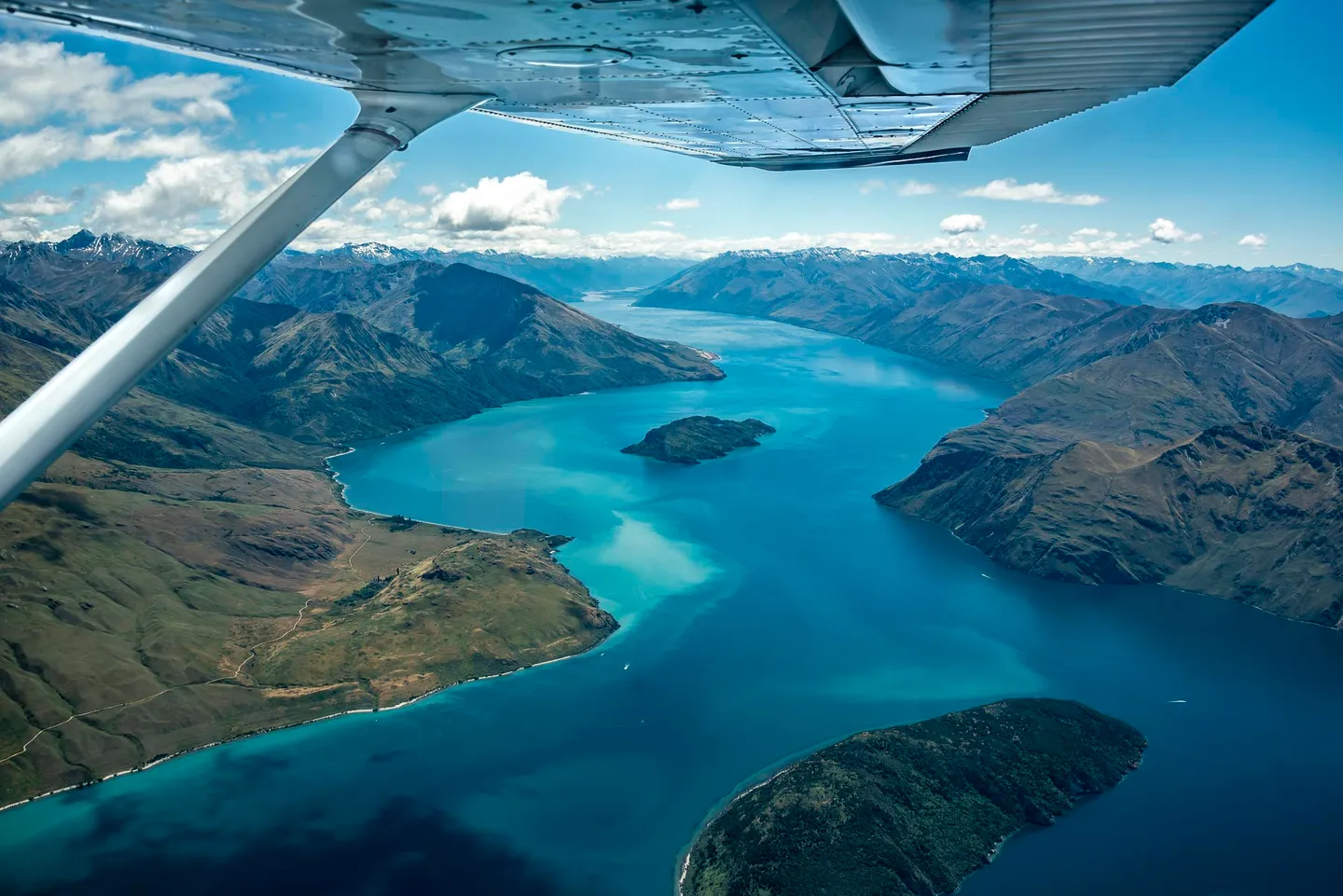 View beneath an aircraft wing across turquoise Lake Wanaka and surrounding mountains.