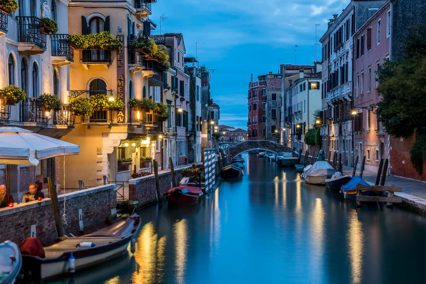 Blue-hour view along a Venetian canal with warm hotel lights reflected in the water.