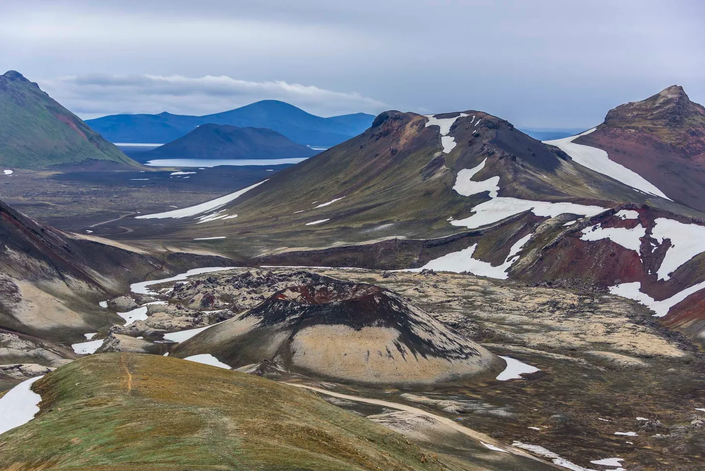 Layered volcanic mountains with lingering snowfields beneath a pale sky.