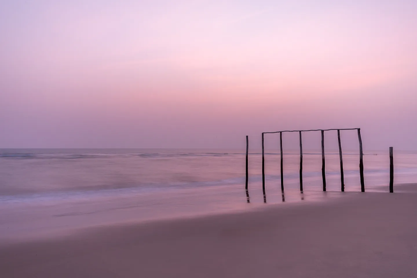 A long-exposure sunset over Nungwi Beach with wooden posts at the shoreline.