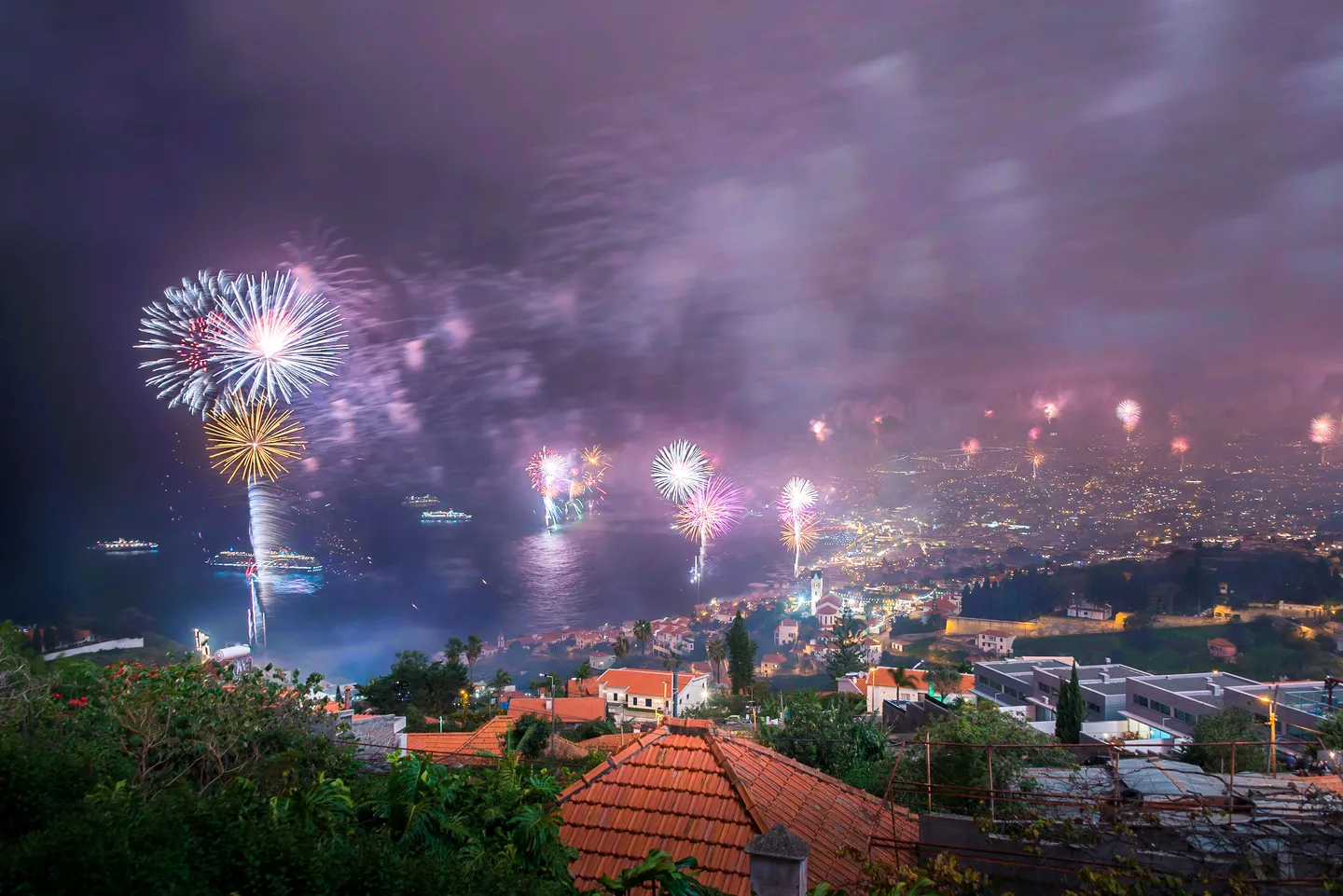 Fireworks illuminating Funchal and its harbor at night.